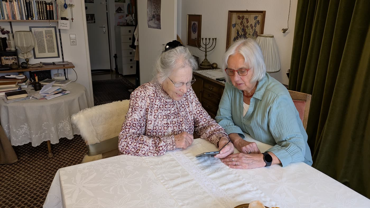 Eine Vertrauensperson sitzt mit einer Seniorin am Wohnzimmertisch