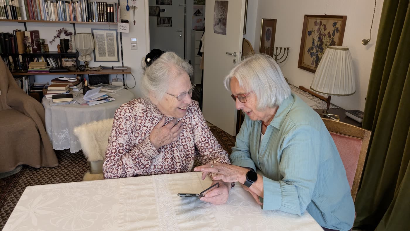 Eine Mentorin erklärt einer Seniorin zu Hause die Bedienung des Smartphones