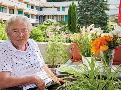 Eine Bewohnerin sitzt auf ihrem bepflanzten Balkon